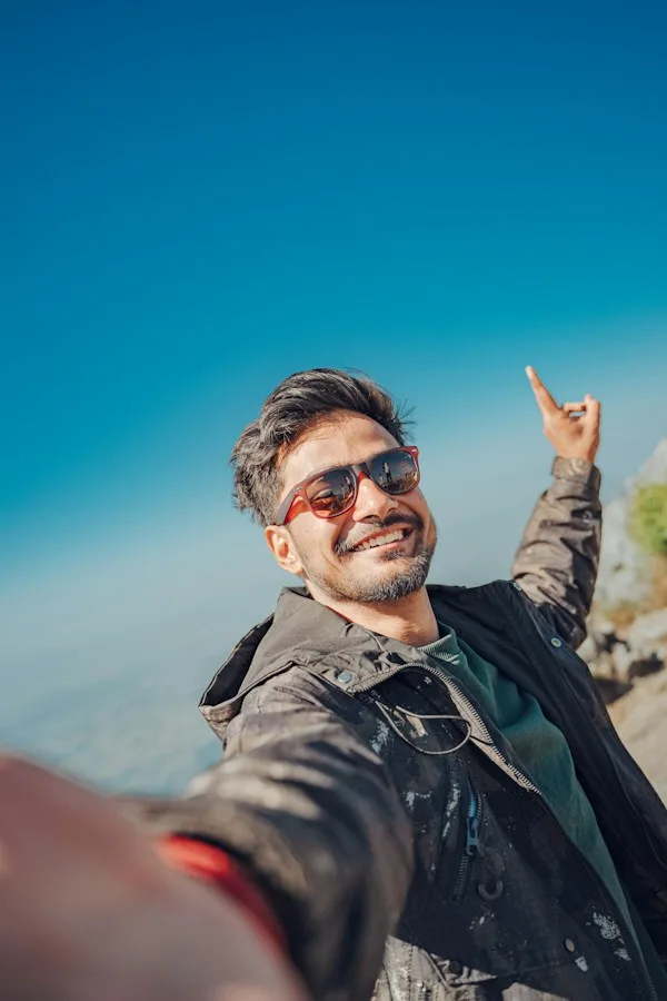 Smiling man in sunglasses taking a selfie against a clear blue sky